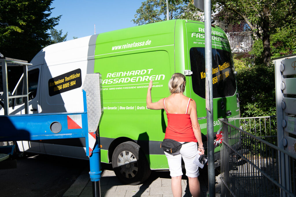 Grün weißer Transporter der Firma Reinhardt Fassadenrein bei rückwärts einparken vor einem Objekt