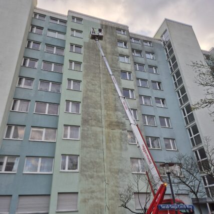Hochhaus mit einem Kranfahrzeug von welchem aus gerade die Fassade des Hauses gereinigt wird